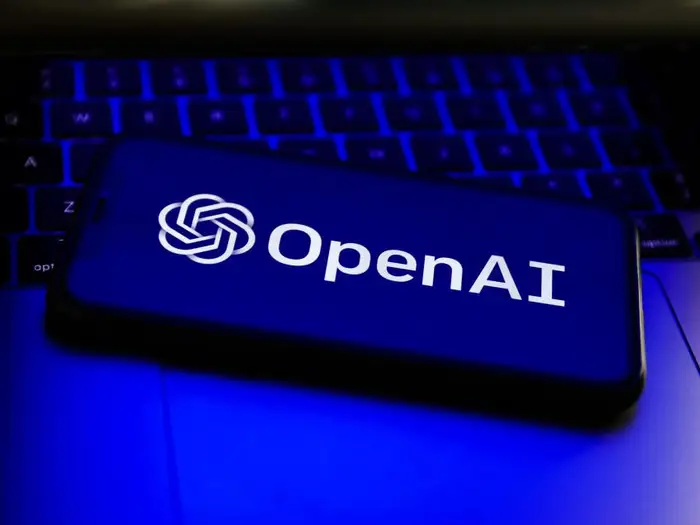 A Cell Phone placed on a laptop on which OpenAI is written
